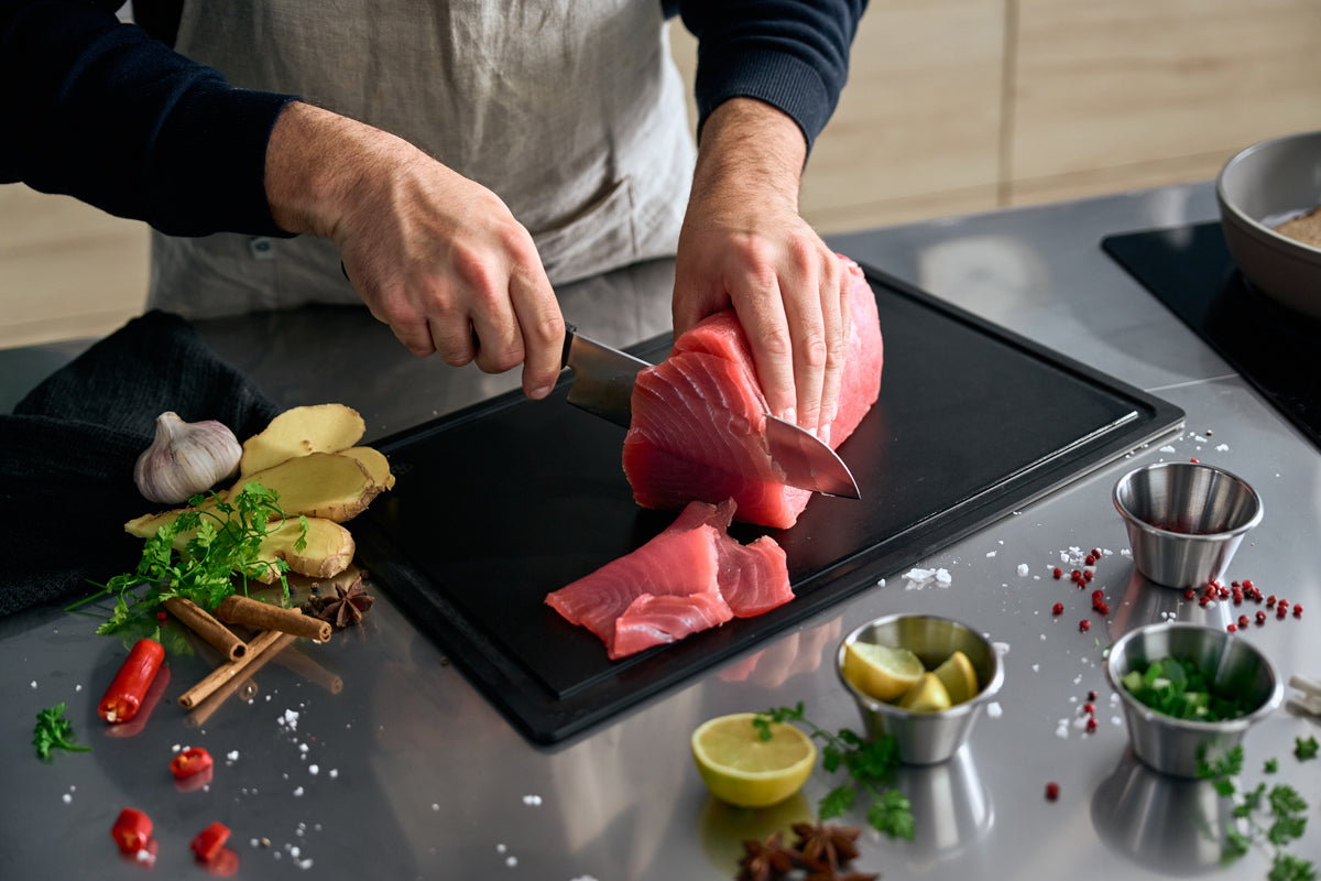 Preparing fresh tuna with the Fissler ProCut Santoku knife 17cm on a simple black cutting board, surrounded by herbs and spices - precision made in Germany.