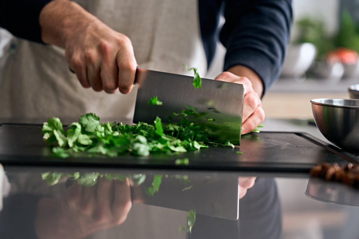 A person cuts herbs on a black cutting board with the Fissler ProCut Chinese Chef's Knife, showcasing German precision and modern design.
