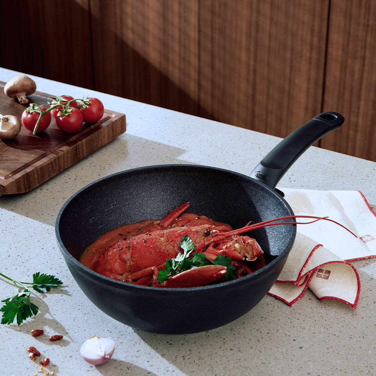 A lobster cooked in sauce is elegantly presented in the Fissler Adamant® wok, expertly made in Germany by Fissler since 1845. The scratch-resistant nonstick coating ensures easy release and serving. Parsley, tomatoes, mushrooms, garlic, and a...