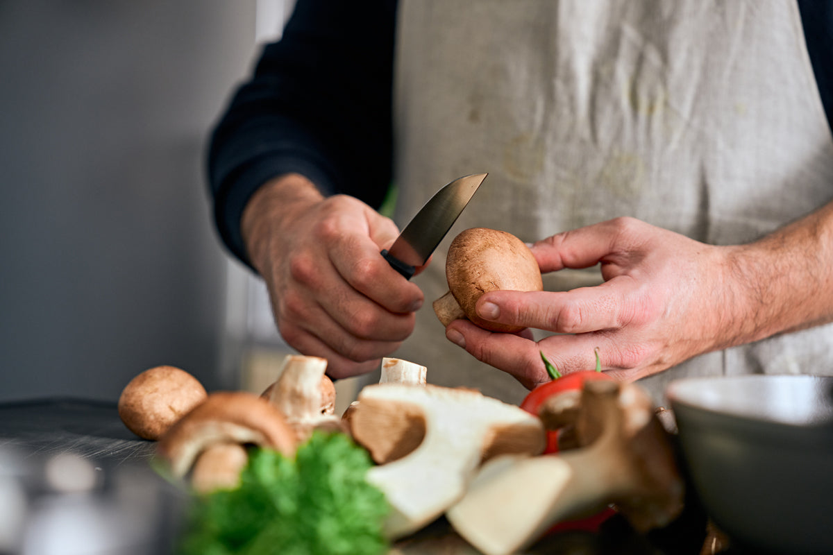 A person in an apron cuts a mushroom with the Fissler ProCut vegetable knife 9cm, with fresh ingredients on a modern counter.
