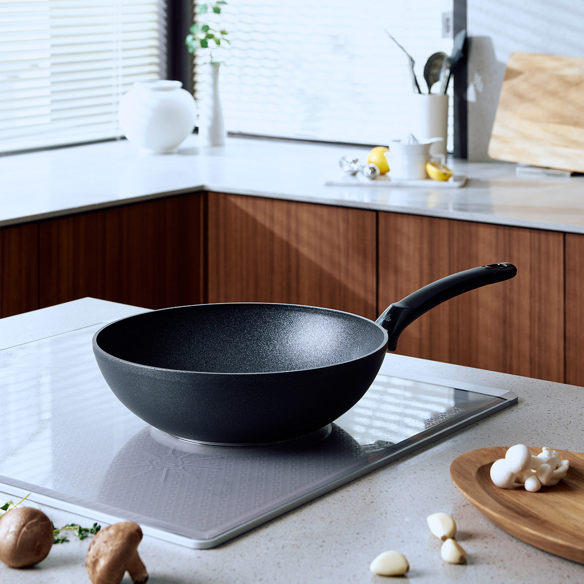The Fissler Adamant® Wokpfanne, crafted with a durable nonstick coating and engineered for exceptional performance, rests on a sleek induction cooktop in a luminous kitchen featuring wooden cabinetry and thoughtfully arranged kitchen accessories. This scene highlights Fissler’s renowned German precision, innovative design, and enduring quality since 1845—hallmarks found across our complete range of pots, pans, pressure cookers, and premium kitchen tools.