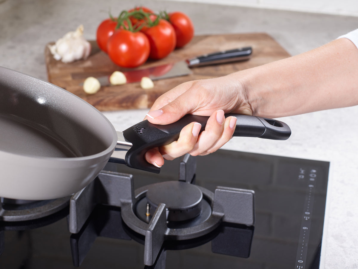 A black handle is attached to a Fissler Ceratal® pan, which is on a gas stove, with fresh ingredients and quality made in Germany.
