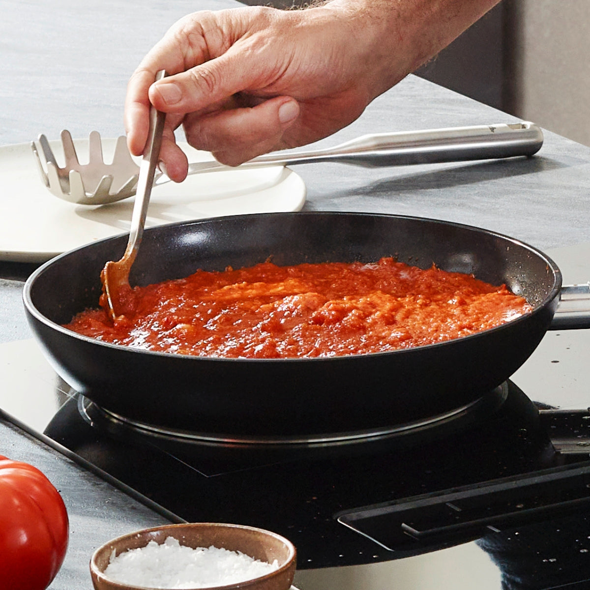 A hand stirs tomato sauce in a Fissler Essential® pan on the stove - modern, PFAS/PTFE-free, quality "Made in Germany".
