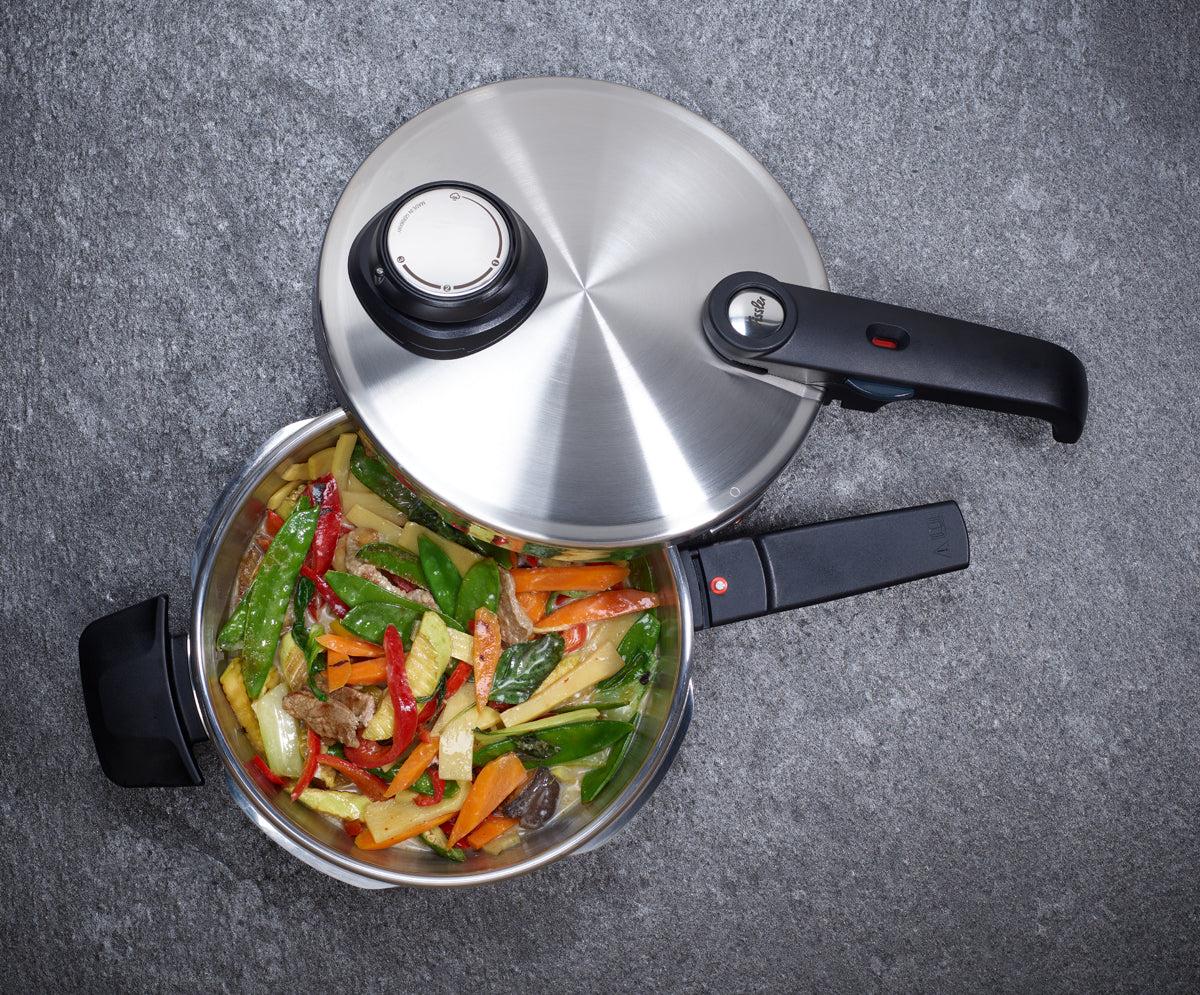 Fissler Vitavit® Premium Schnellkochtopf aus Edelstahl mit gegartem Gemüse und Rindfleischstreifen auf grauer Oberfläche.