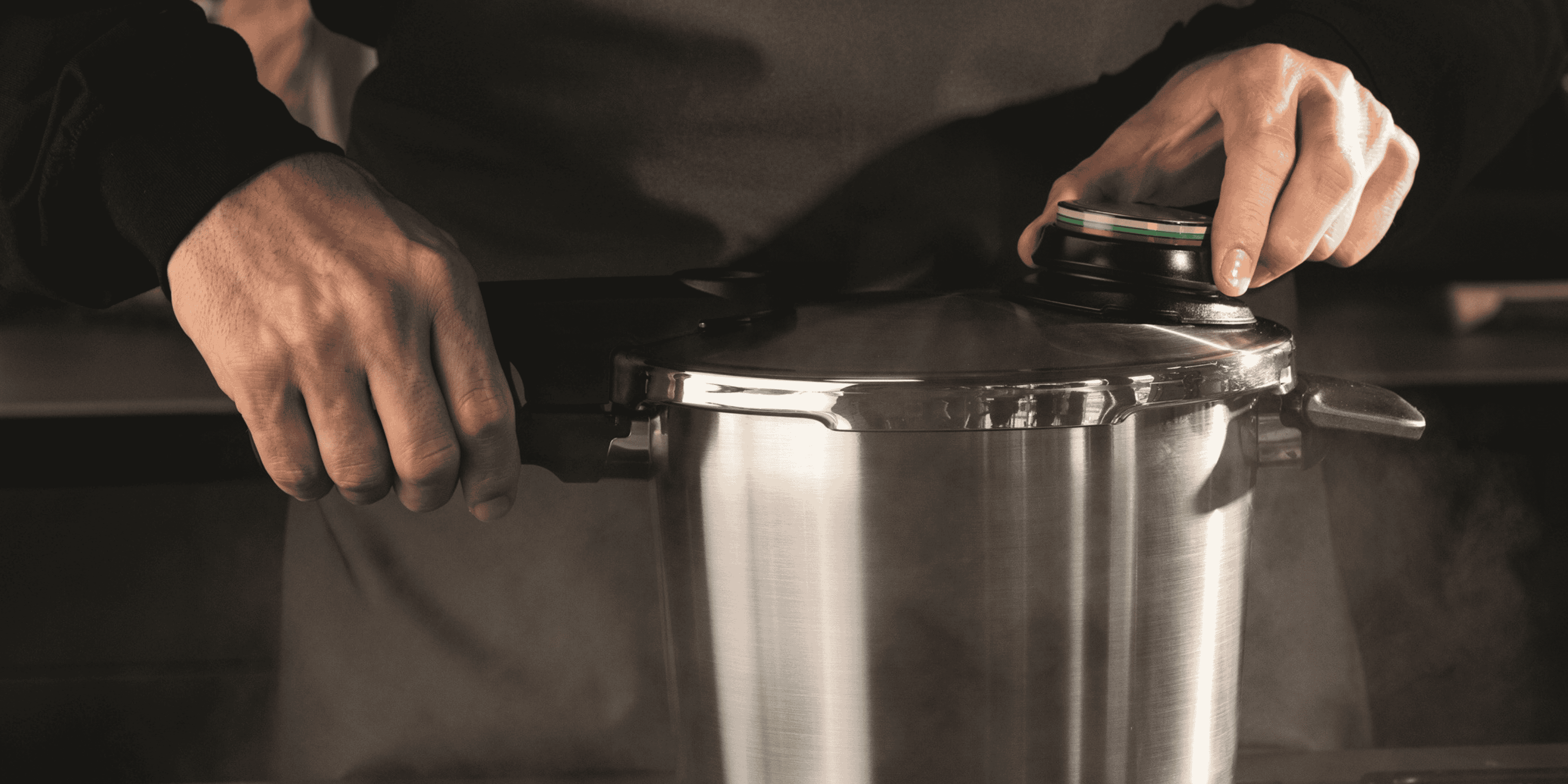 Hände betätigen den Deckel eines Fissler Schnellkochtopfes aus Edelstahl, der in einer modernen Küche Dampf ablässt und deutsche Präzision demonstriert.