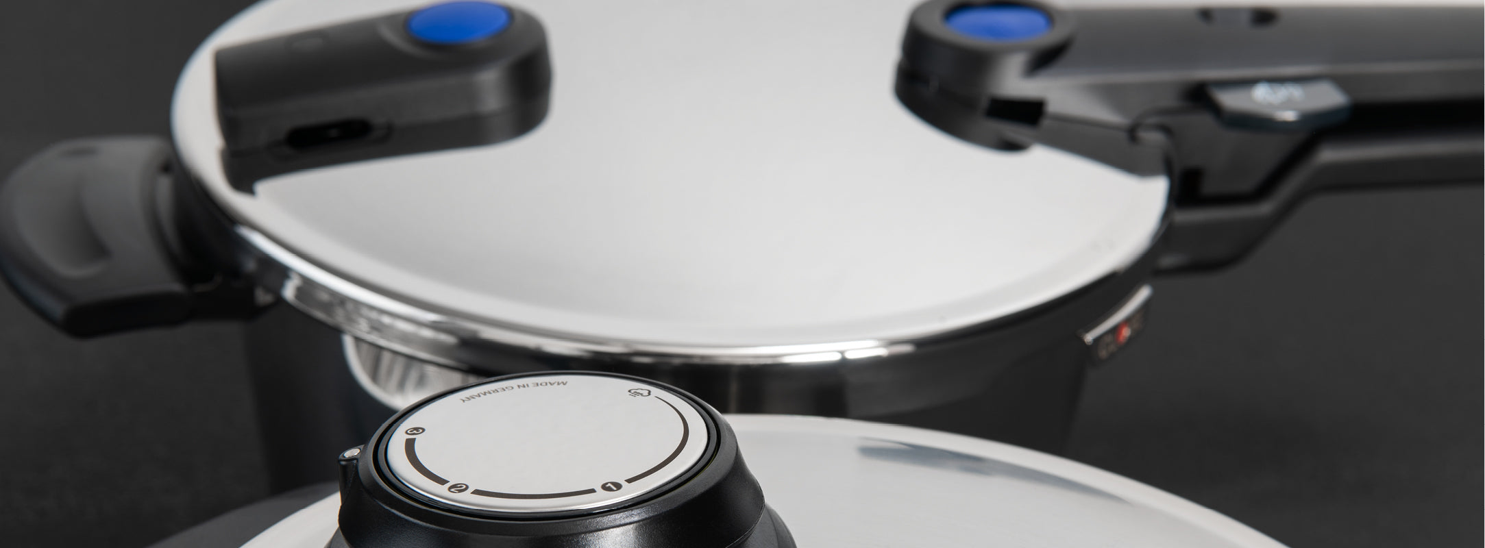 Nahaufnahme von zwei Fissler Schnellkochtopfdeckeln aus Edelstahl mit ergonomischen schwarzen und blauen Griffen, die deutsche Handwerkskunst demonstrieren.