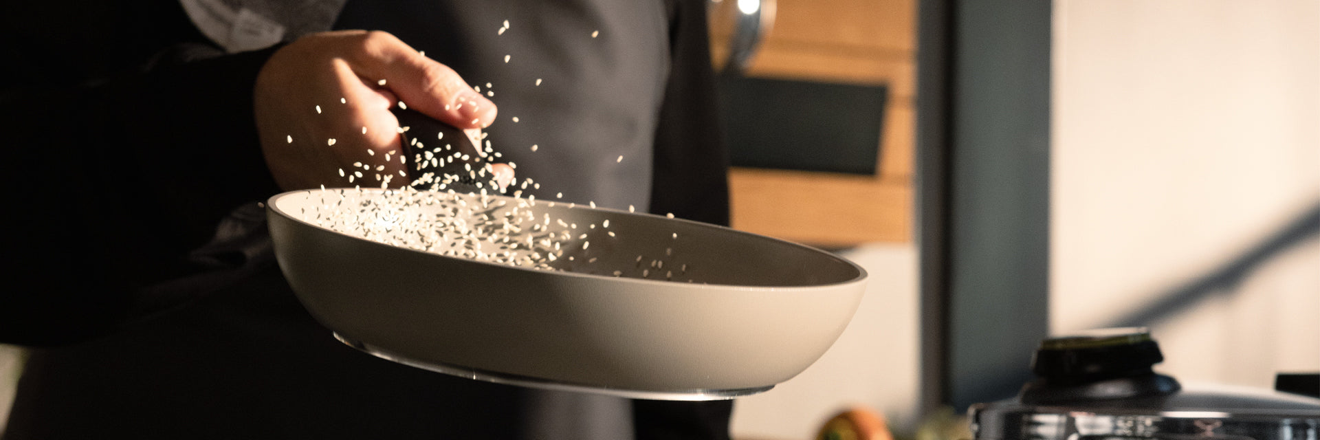 Eine Köchin schwenkt gekonnt ungekochten Reis in einer beigen Fissler-Pfanne und zeigt damit deutsche Qualität und Innovation in der Küche.