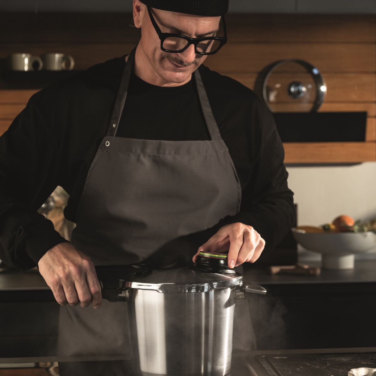 A person in a modern kitchen carefully opens a Fissler stainless steel pressure cooker, releasing steam – precision and quality in action.