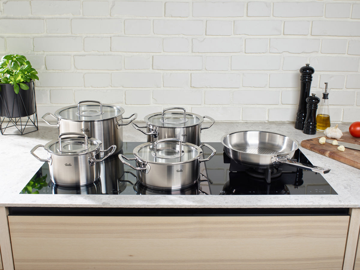 Fissler Original-Profi Collection® 5-tlg. Set auf Induktionskochfeld, weiße Wand, Schneidebrett mit Gemüse und Gewürzen.