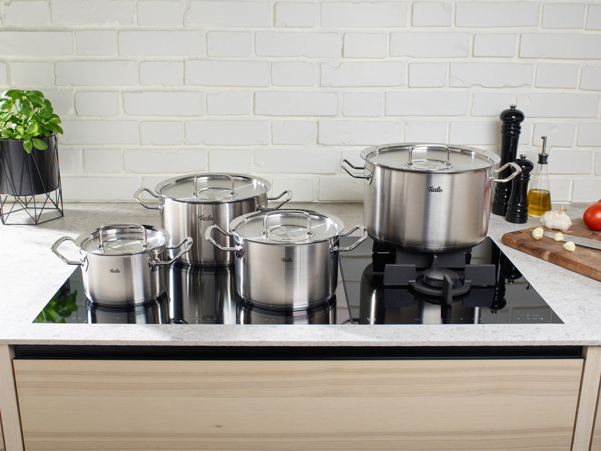 Fissler Original-Profi Collection® Töpfe mit Deckel auf dem Induktionsherd; im Hintergrund: weiße Fliesen, frisches Gemüse und Küchenzubehör.