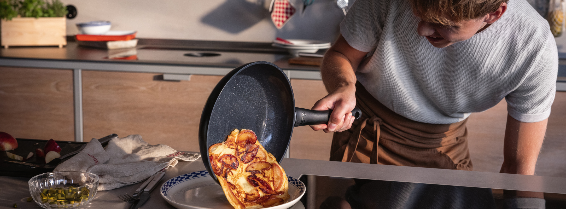 A person expertly slides a golden omelette from a Fissler Frying Pan onto a plate; premium Cookware and utensils sit on the countertop.