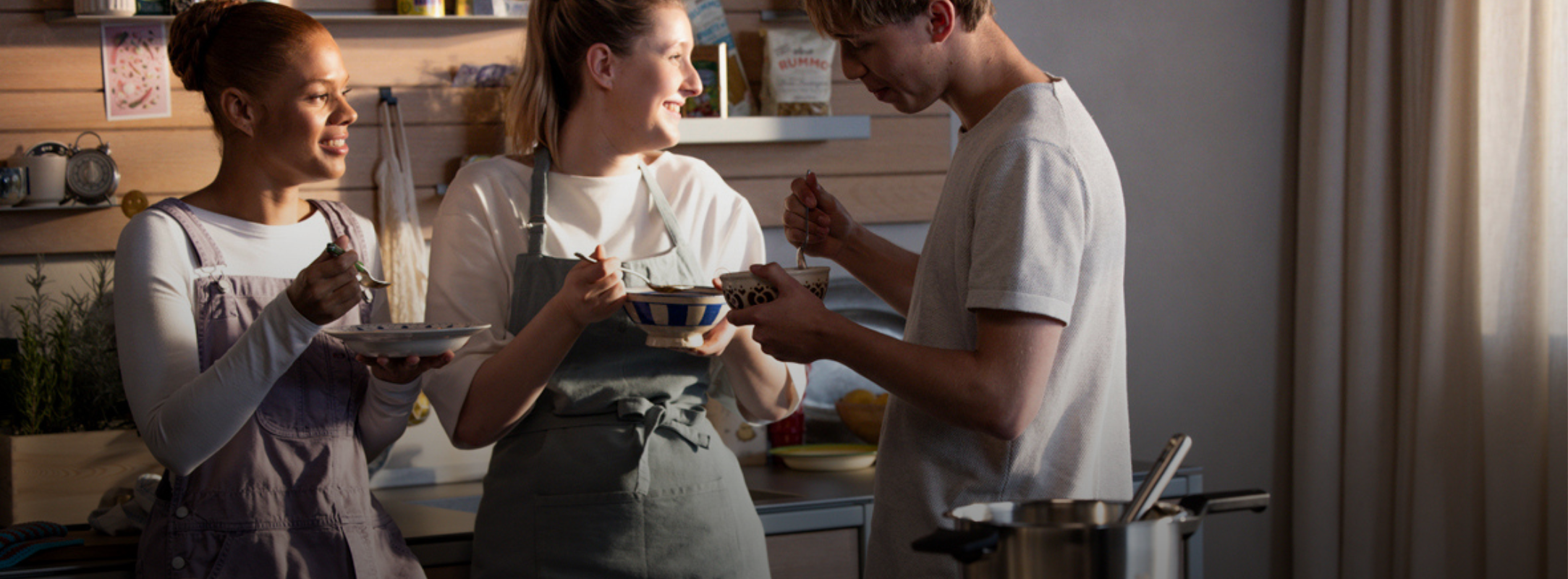 Three people enjoy a meal in a sunlit kitchen featuring Fissler stainless steel cookware, highlighting timeless quality and German design.