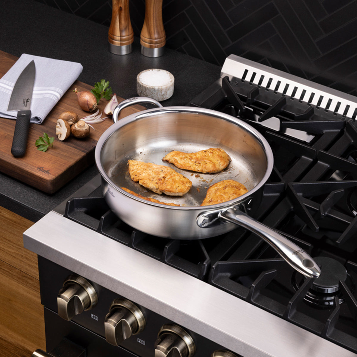 Three pieces of chicken breast are sizzling in a Fissler M5 Pro-Ply® Sautépfanne mit Metalldeckel on a gas stove, showcasing the precision engineering and durability of our Made in Germany stainless steel cookware. Next to the stove, a cutting board displays a high-quality Fissler knife alongside fresh mushrooms, parsley, and a neatly folded towel. The scene is set against a modern kitchen with an elegant black backsplash, reflecting Fissler’s commitment to timeless design and innovation since 1845.