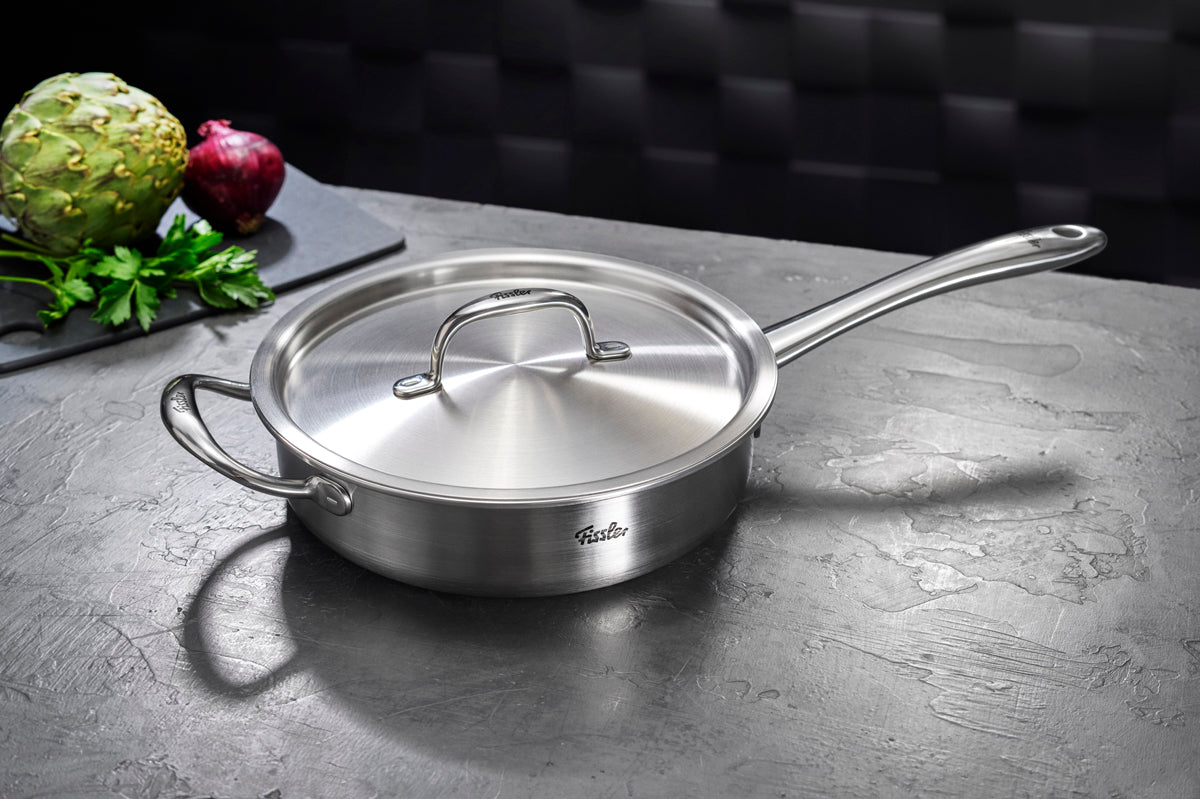 Fissler M5 Pro Ply® 4-piece sauté pan with lid on a gray countertop, with fresh vegetables in the background on a black cutting board.