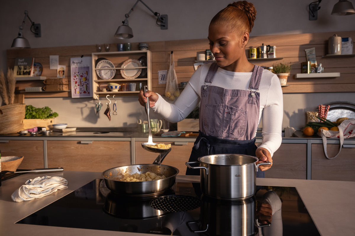 A woman is cooking in a modern kitchen with a Fissler Pure Collection Cooking Pot with Glass Lid - precision craftsmanship from Germany - on the stove.