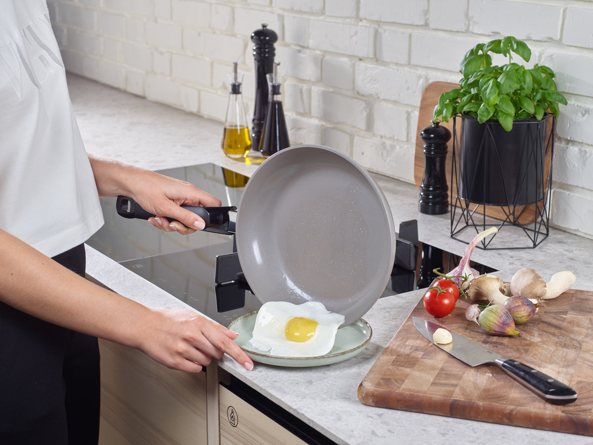 A fried egg slides from the Fissler Ceratal® Classic pan set onto a plate in a modern kitchen, with Fissler quality tools next to it.
