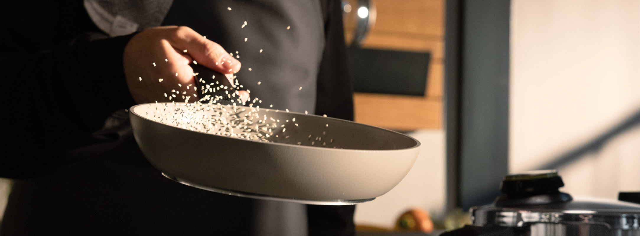 Ein Koch schwenkt gekonnt Reis in einer hochwertigen Fissler-Pfanne und zeigt deutsche Präzision in einer modernen Küche mit Holzschränken.