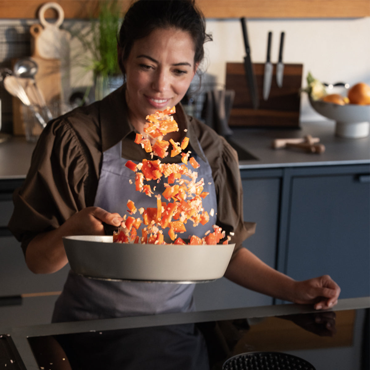 A woman uses a Fissler Ceratal® Evo Comfort pan set, tossing vegetables with joy in a modern kitchen—precision made in Germany.