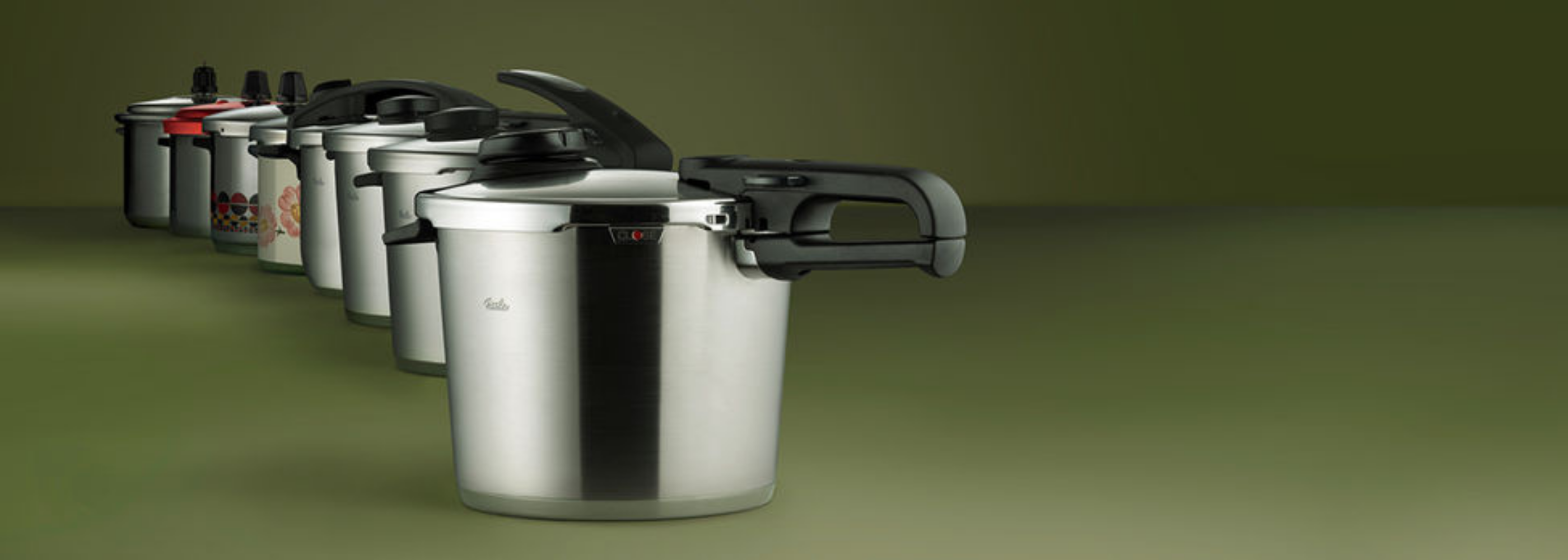 Six Fissler stainless steel pressure cookers in a diagonal row, each with a unique, German-engineered lid and handle design.