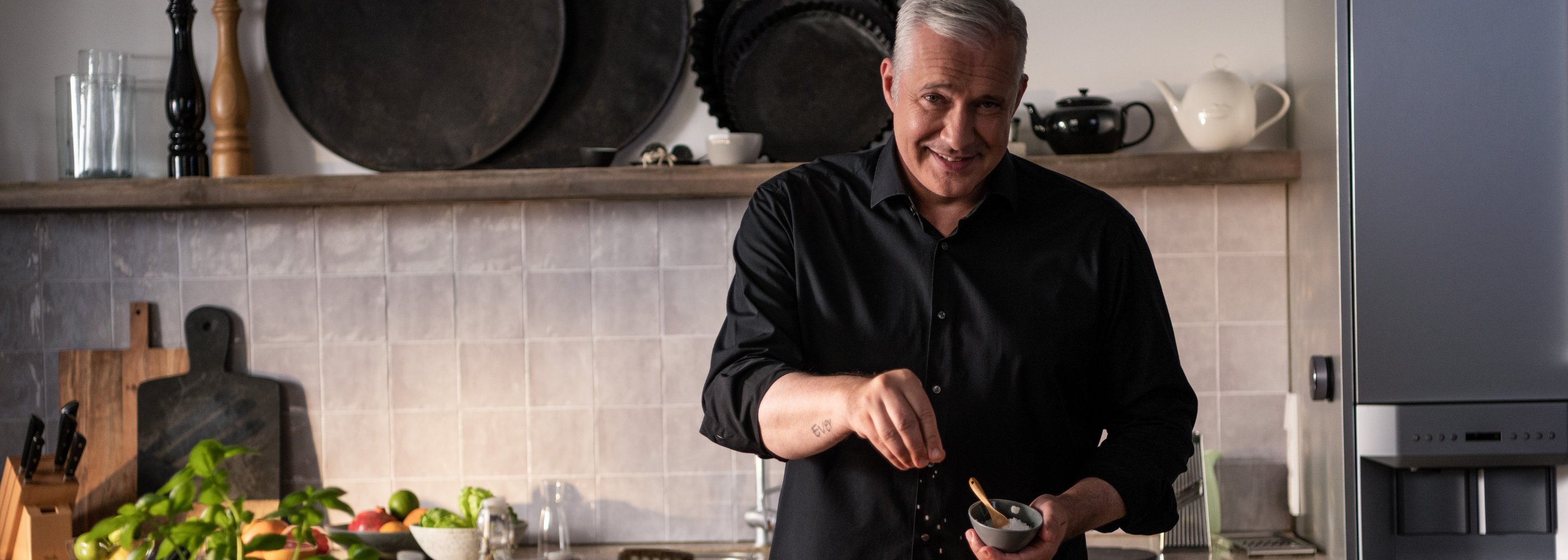 A man in a black shirt prepares food in a modern kitchen with high-quality Fissler cookware and fresh vegetables on the counter.