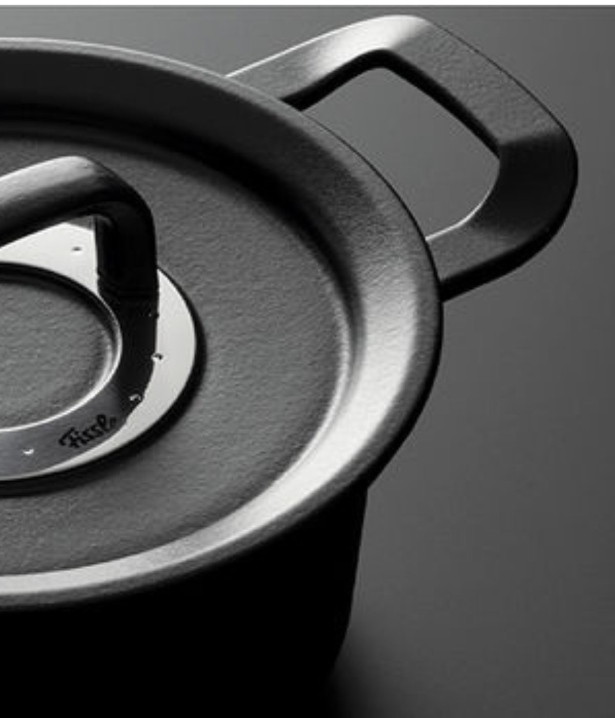 Close-up of a black Fissler pot with lid and sturdy metal handle, showcasing timeless German design and precision on a dark surface.