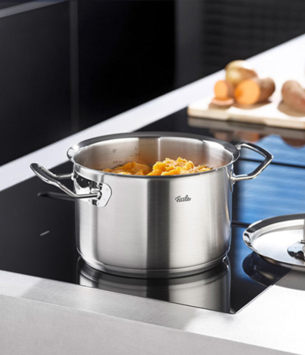 A Fissler stainless steel pot filled with chopped orange vegetables on an elegant induction hob - precision meets timeless design.