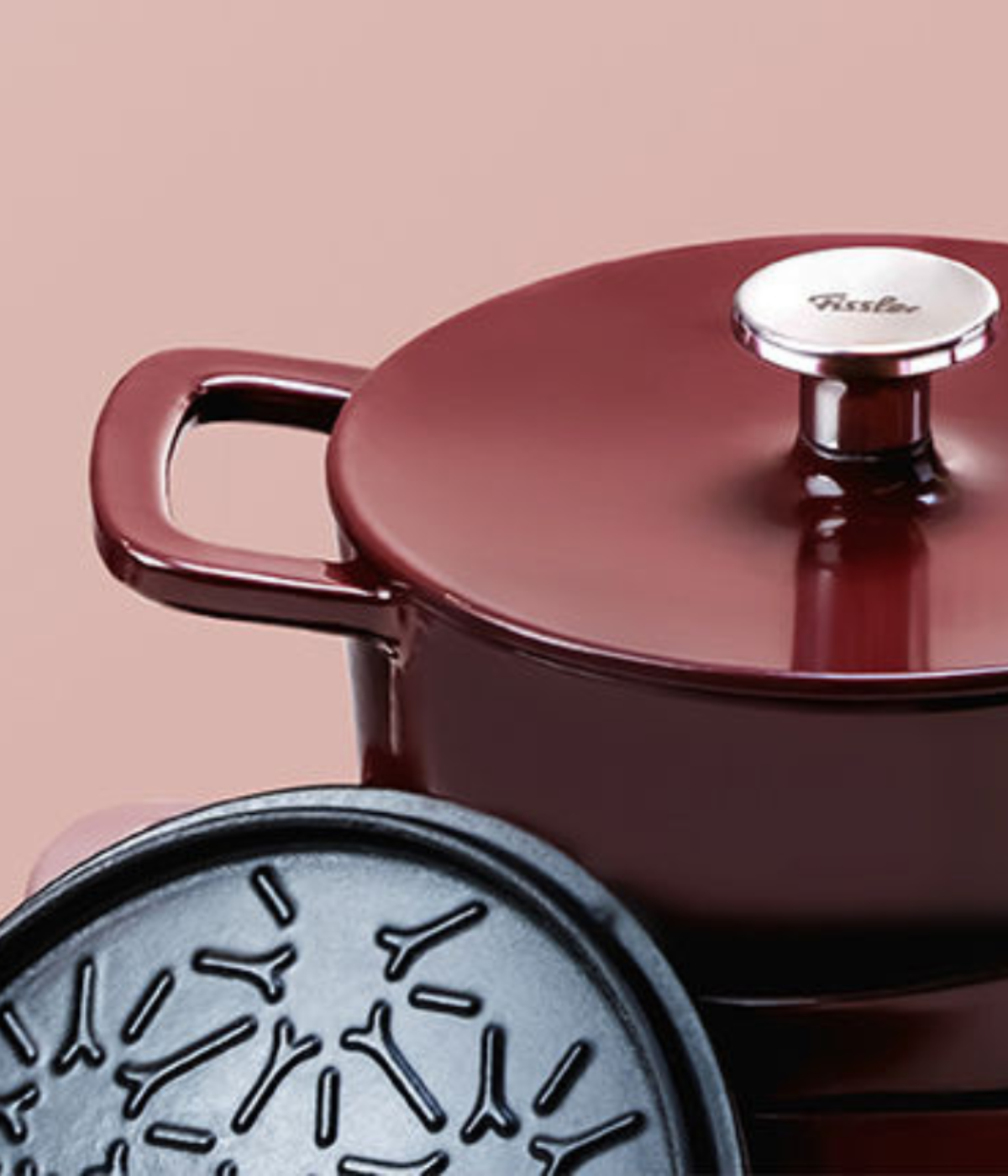 Chestnut brown Fissler cast iron pot with matching lid, shiny finish, and sturdy handle, behind a coaster on a soft pink background.
