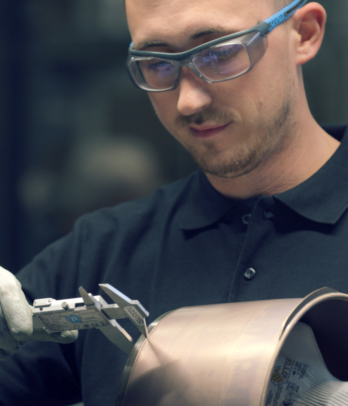 A craftsman wearing safety glasses and gloves measures a stainless steel pot part, demonstrating German precision engineering from Fissler.