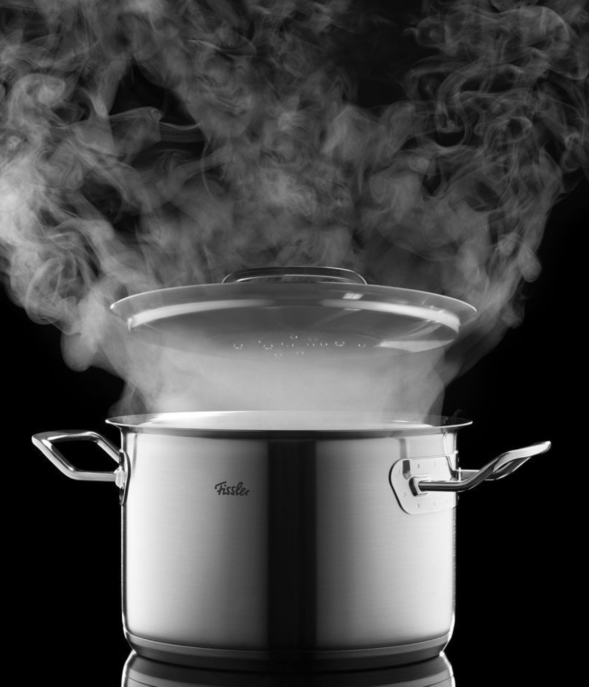 A Fissler stainless steel pot with a glass lid lets steam escape, highlighting German precision and timeless design against a black background.