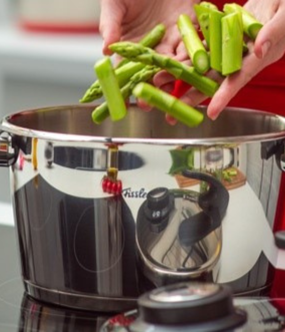 A person prepares to add sliced asparagus to a Fissler stainless steel pot on the stove, showcasing German quality cookware.