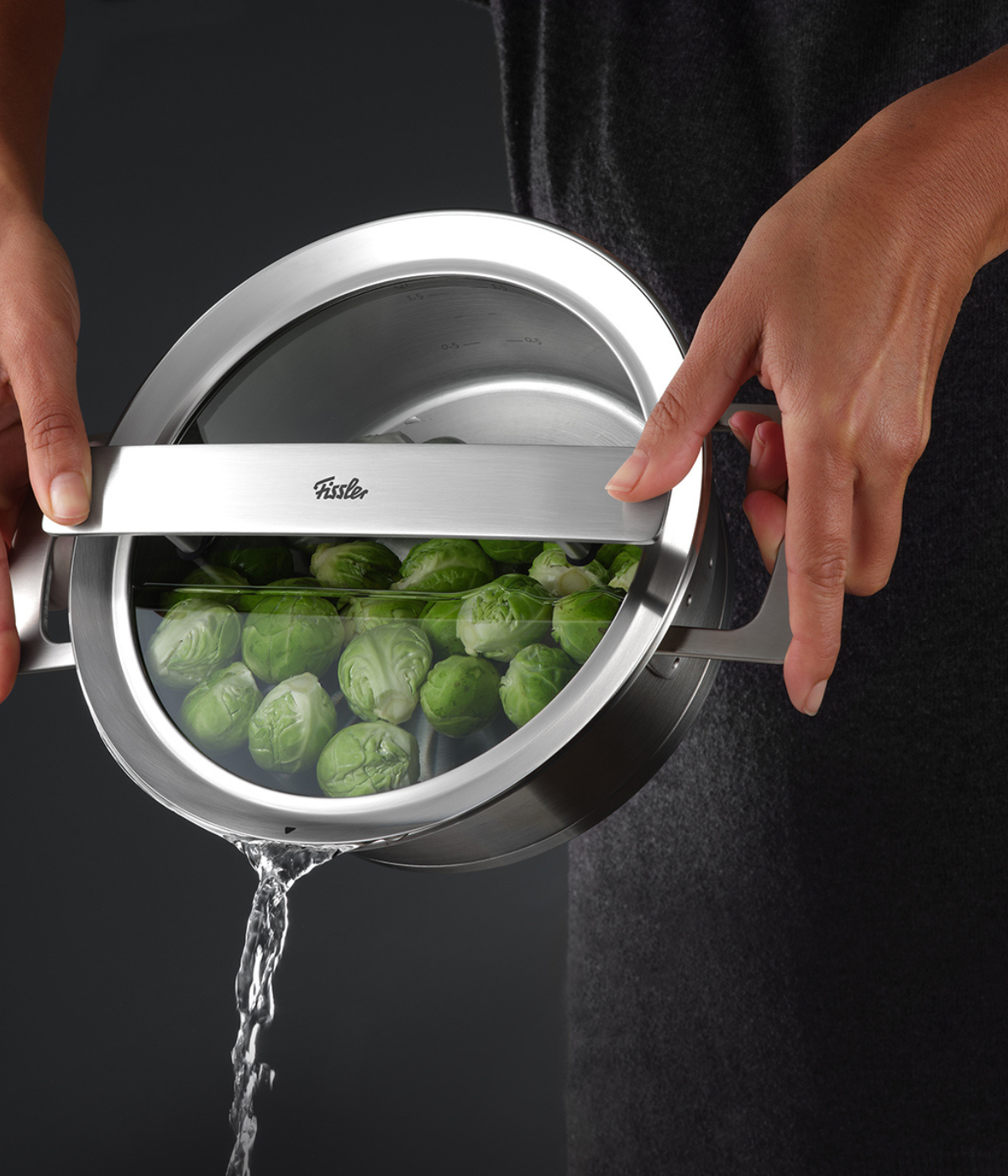 A person drains Brussels sprouts from a Fissler stainless steel pot, with the precision-engineered lid allowing for a seamless, controlled pour.