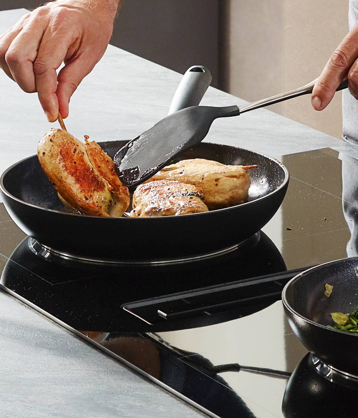 A chef prepares a stuffed chicken in an elegant Fissler Frying Pan on an electric stove; next to it is a Fissler Frying Pan with fresh greens.