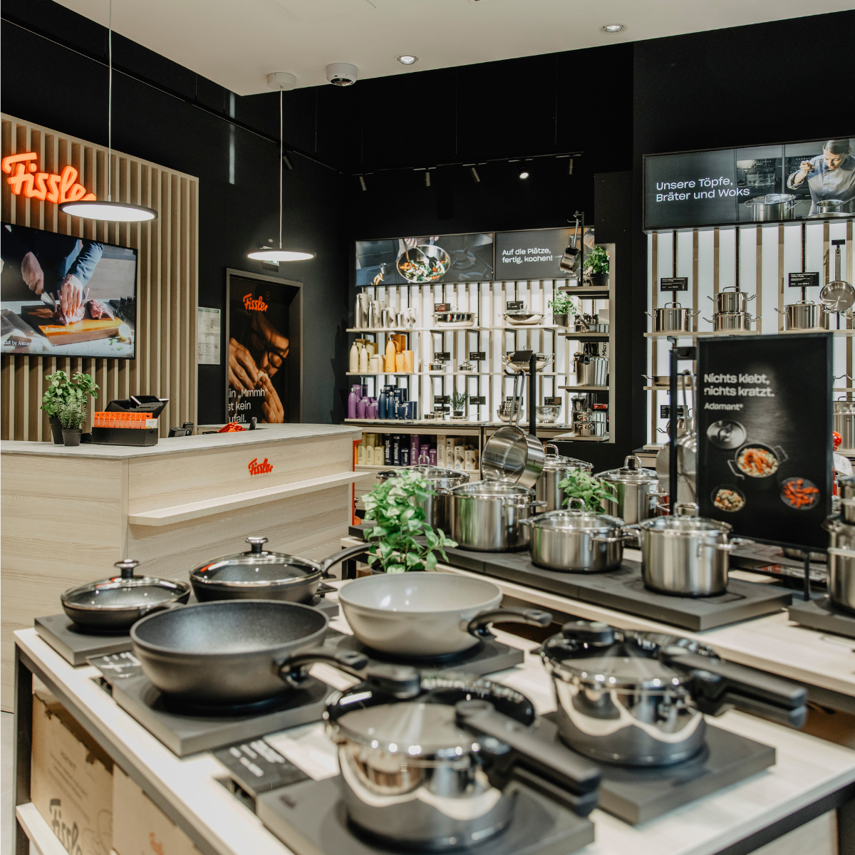 In einem Fissler-Küchenfachgeschäft werden unsere hochwertigen Töpfe, Pfannen, Schnellkochtöpfe und Küchenaccessoires aus Edelstahl auf elegant gestalteten Theken und Regalen präsentiert. Helle Beleuchtung bringt die langjährige Handwerkskunst und das zeitlose Design jedes einzelnen Stücks besonders gut zur Geltung. Schilder mit deutschen Texten und Bildern spiegeln die Tradition von Fissler wider, die seit 1845 von Präzisionstechnik und Innovation geprägt ist.