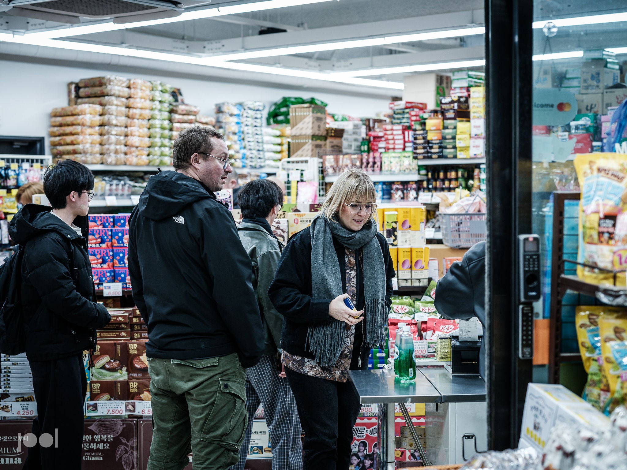 Customers queue in a well-lit specialty store featuring Fissler’s premium cookware collection. The woman at the front selects precision-engineered stainless steel pots and pans, while others await their turn among shelves artfully arranged with Fissler pressure cookers and durable kitchen accessories, each representing German innovation and timeless design.